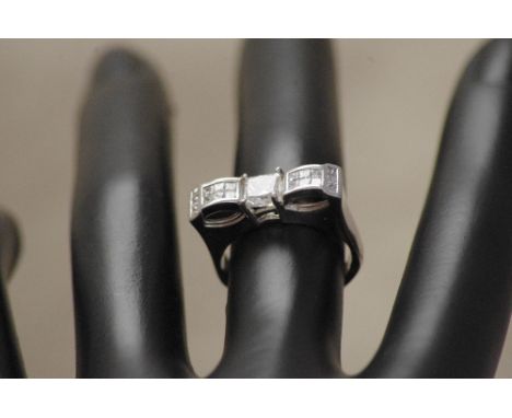 A 18ct white gold diamond ring, the central square cut diamond flanked by 18 diamonds in a buckle style setting. Approximate 