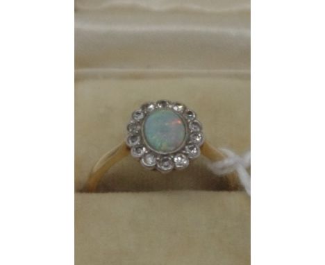 An 18ct gold and platinum set opal and diamond dress ring, the central opal surrounded by 14 diamonds of similar size. Approx