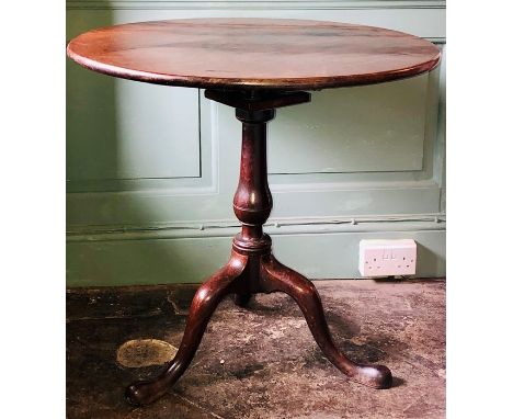 A George III oak pedestal tilt top table, circa 1820, circular top on a turned column, raised cabriole tripod legs and padded