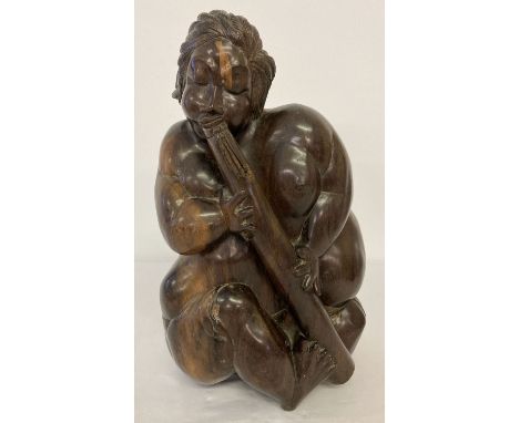 A heavy hardwood carved figure of a tribesman playing a pipe.  Approx. 30cm tall.