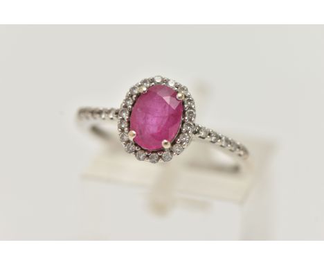 AN 18CT WHITE GOLD RUBY AND DIAMOND RING, set with an oval cut ruby, in a halo of round brilliant cut diamonds, and diamond s