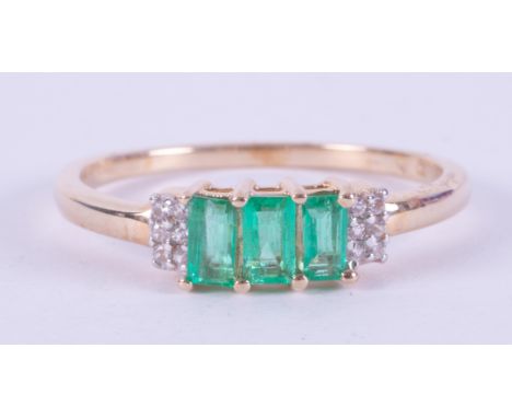 A 9ct yellow gold ring set with three baguette cut Colombian emeralds, total weight 0.55 carats with six round cut white zirc