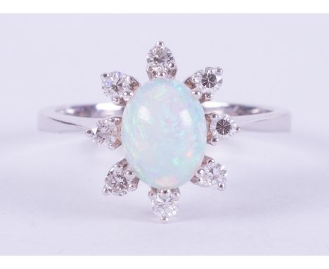 An 18ct white gold cluster ring set with a central oval cabochon cut white opal measuring approx. 8mm x 6mm, surrounded by ei