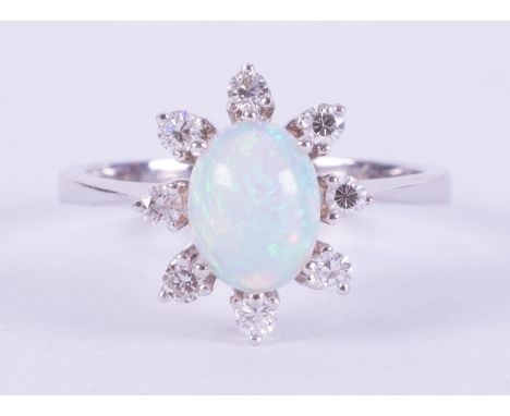 An 18ct white gold cluster ring set with a central oval cabochon cut white opal measuring approx. 8mm x 6mm, surrounded by ei