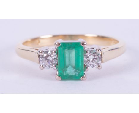 An 18ct yellow &amp; white gold three stone ring set with a central emerald cut emerald, approx. 0.65 carats with a round bri