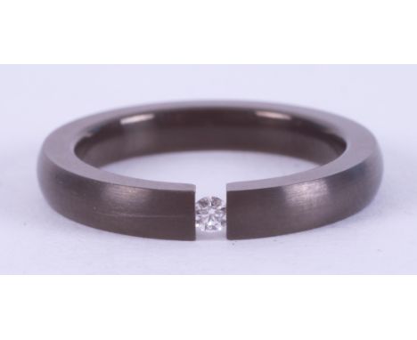 A titanium band with a tension set 0.03 carat round brilliant cut diamond, 3mm x 2.6mm, 1.77gm, size K.