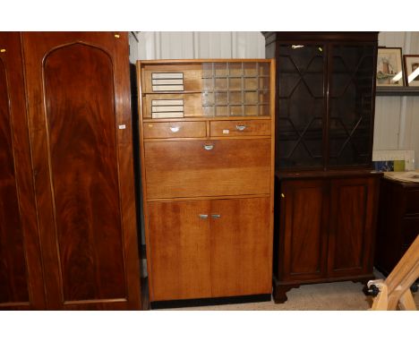 A light oak retro kitchen cabinet, the glazed upper section above two drawers, drop flap compartment and cupboards below