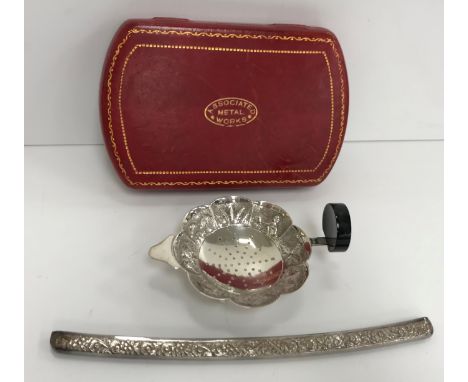 An Eastern (possibly Thai or Burmese) embossed white metal tea strainer and stand with figural and tree decoration, together 