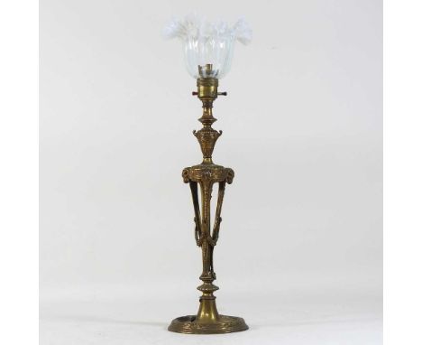 An early 20th century gilt metal table lamp, decorated in relief with rams heads and festoons, with a frilled opaline glass s