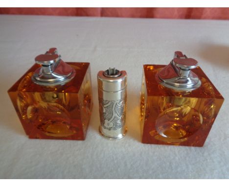 A white base metal lighter together with 2 glass cube shaped table lighters , chipping to corners of glass cubes (3)