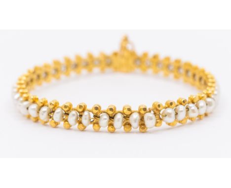 A yellow metal and pearl set hinged bangle a/f split, set with a central row of cultured pearls within a faceted beaded borde
