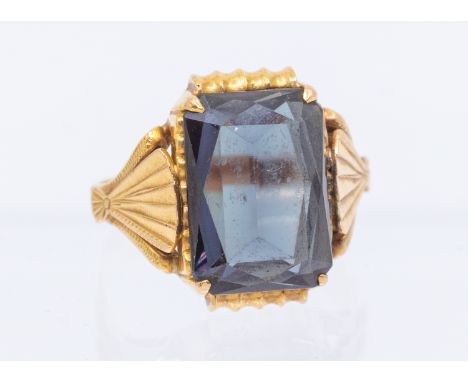 A synthetic sapphire and gold cocktail ring, comprising a rectangular scissor cut stone approx 13 x 10mm, shell decoration to
