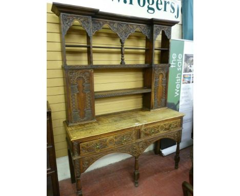 An early 20th Century Flemish style oak dresser, the open back Delft rack with stepped cornice over a floral and leaf carved 