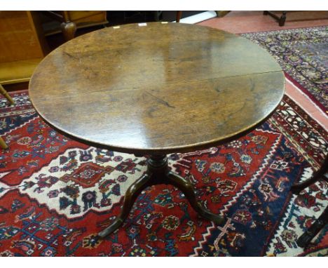 An antique oak tilt top table with a well coloured 74 cms diameter top on a turned column tripod base, 70 cms high