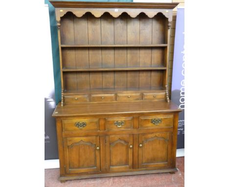 A reproduction oak dresser, the three shelf plate rack with planked back and shaped frieze under a moulded cornice with spice