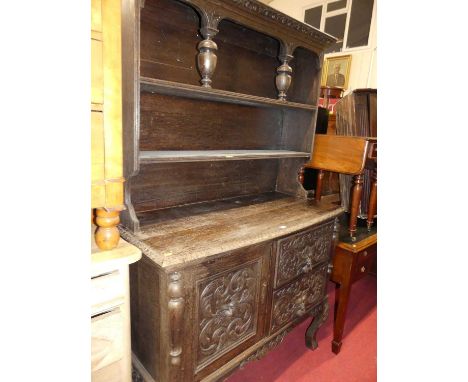 An early 20th century heavily relief carved oak dresser, having two-tier open shelf over base fitted with two drawers and sin