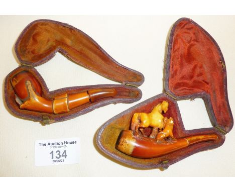 Two carved Meerschaum smoking pipes, one decorated with horse and dog, the other formed as a hand holding an egg. Both cased 