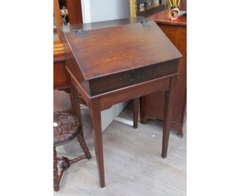 An early 18th Century oak desk on stand the rising slope and shelf interior over square tapering legs with carved central mot