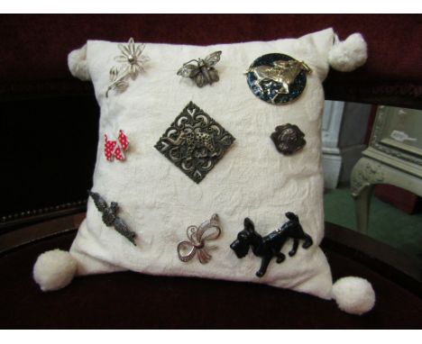 A cushion with a selection of brooches including Sterling silver and a Moulin Rouge example