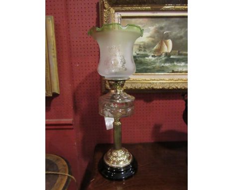 A late Victorian oil lamp with black ceramic base, brass column to clear reservoir, frosted glass shade