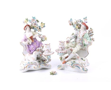 A pair of Samson candlestick figures. Circa 1900, in the Derby style, each with a reclining figure against flowering branches