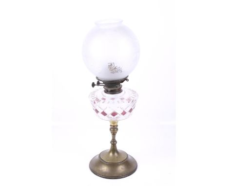 A Victorian oil lamp. Having an etched glass shade, cut glass reservoir with red details and a brass stand with a circular ba