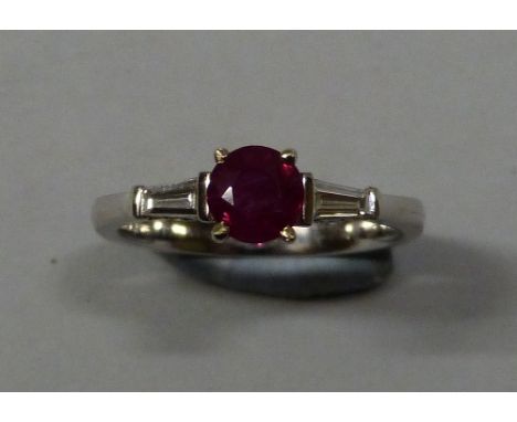 An 18k white gold, ruby and diamond three stone ring, claw set with a round ruby weighing approximately 0.60cts, flanked by t