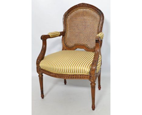Fauteuil, Louis XVI. Geschnitztes Nussbaumgestell auf kannelierten Beinen. Sitz mit Streifenbezug, Rücken mit Korbgeflecht. F