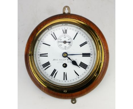Brass bulkhead clock by John Lilley and Son, London, on an oak back, with key, the clock approximately 22cm diameterCondition
