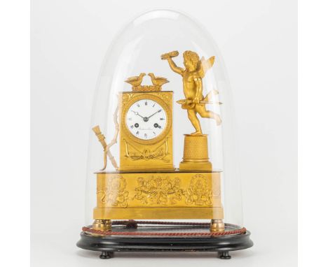 A gilt mantle clock in empire style with putti and doves, standing under a glass dome. The first half of the 19th century. Ha