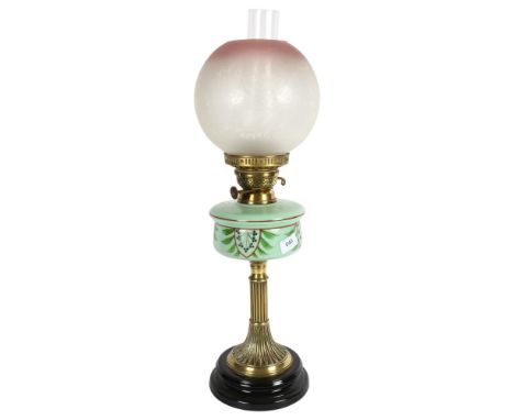 A Victorian brass oil lamp, with a cranberry and clear glass etched shade and painted green glass font, on black ceramic foot