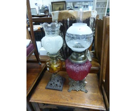 Two iron based antique oil lamps one with a beaded ruby glass reservoir and one other with an amber reservoir