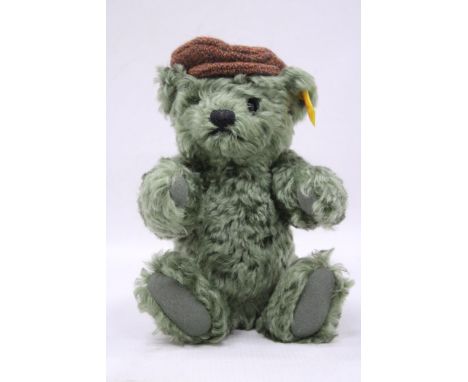 A SMALL GREEN STEIFF THURSDAY TEDDY BEAR WITH A FLAT CAP AND BUTTON TO HIS EAR, HEIGHT 25CM