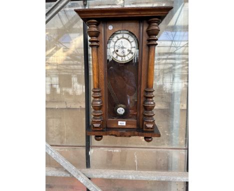AN OAK CASED WALL CLOCK WITH WHITE ENAMEL FACE AND ROMAN NUMERALS COMPLETE WITH KEY AND PENDULUM.