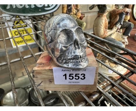A SMALL CAST ALLOY SKULL ON A WOODEN BASE