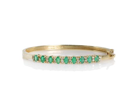 An emerald and diamond hinged bangle, with nine oval mixed cut emeralds interspaced with pairs of round brilliant cut diamond