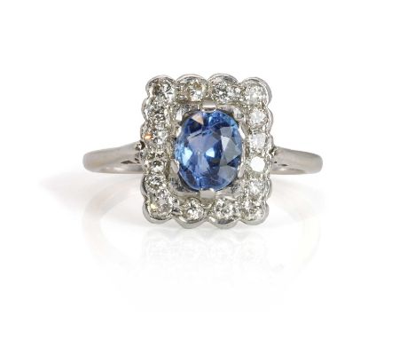 A white gold sapphire and diamond cluster ring,  with an oval mixed cut cornflower blue sapphire within a surround of round b