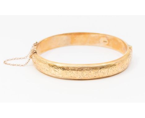 A 9ct gold hinged bangle with foliate engraved decoration, width approx 10mm, internal diameter approx 62mm, safety chain pre