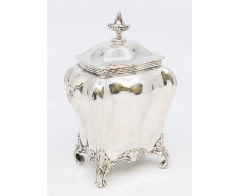 An Edwardian silver tea caddy bombe shaped with four raised scroll and rocaille supports, the hinged cover with stylised fini