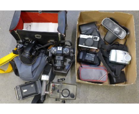 A large black camera box with underwater case and Olympus Trip 35, a black/green case with a Kodak DX3600, a black case with 