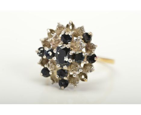 A 9CT GOLD SAPPHIRE AND DIAMOND CLUSTER RING, designed as a central oval sapphire within a tiered circular sapphire and illus