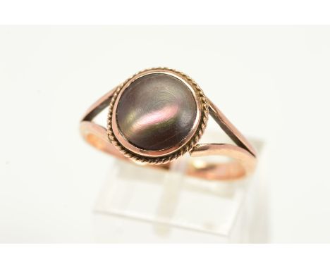AN ABALONE SHELL RING, designed with a circular slice of alabone shell within a rope twist surround to the bifurcated shoulde