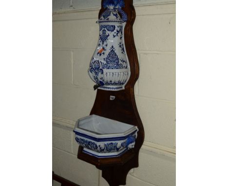 A CONTINENTAL BLUE AND WHITE POTTERY WALL HANGING WATER HOLDER AND BASIN mounted on a wooden frame, height 110cm