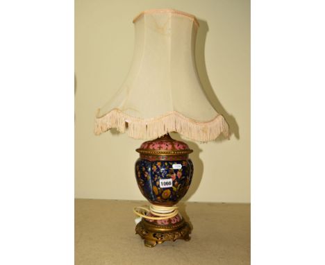 A CERAMIC LAMP BASE HAVING FLORAL AND FOLIATE DECORATION, incorporating a brass and pierced and footed base, brass light fitt