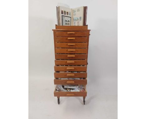 A collection of loose postage stamps housed in a light oak, narrow chest of drawers on legs and castorsHeight 103cm, depth 40