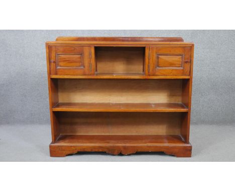 A 20th century cherrywood bookcase, with two cupboard doors centred by a shelf, over two other shelves, on a shaped plinth ba