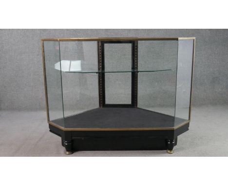 A mid 20th century shop corner display cabinet, glazed, with brass edges, enclosing a single shelf, with a rear door, on an e