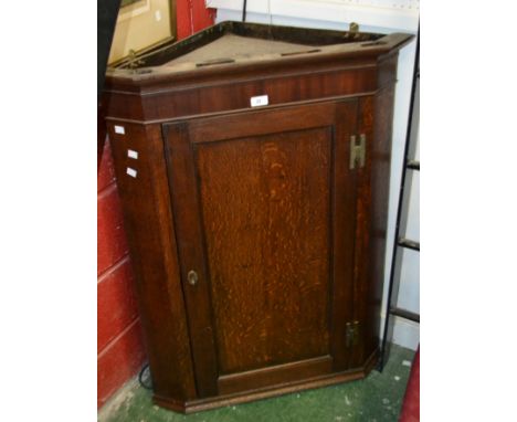 A George III oak splay front wall mounted corner cabinet, outswept cornice, panel door.