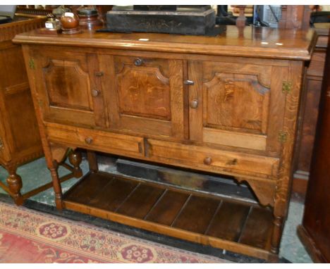 A rustic oak sideboard, oversailing moulded top, fielded panel fall front with rams head carved knob flanked by two fielded d