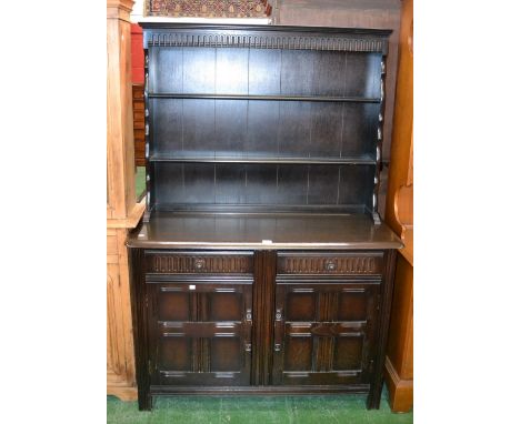 A dark oak Priory dresser, nulled frieze, two shelves, shaped uprights to top, two short drawers over two panel door cupboard